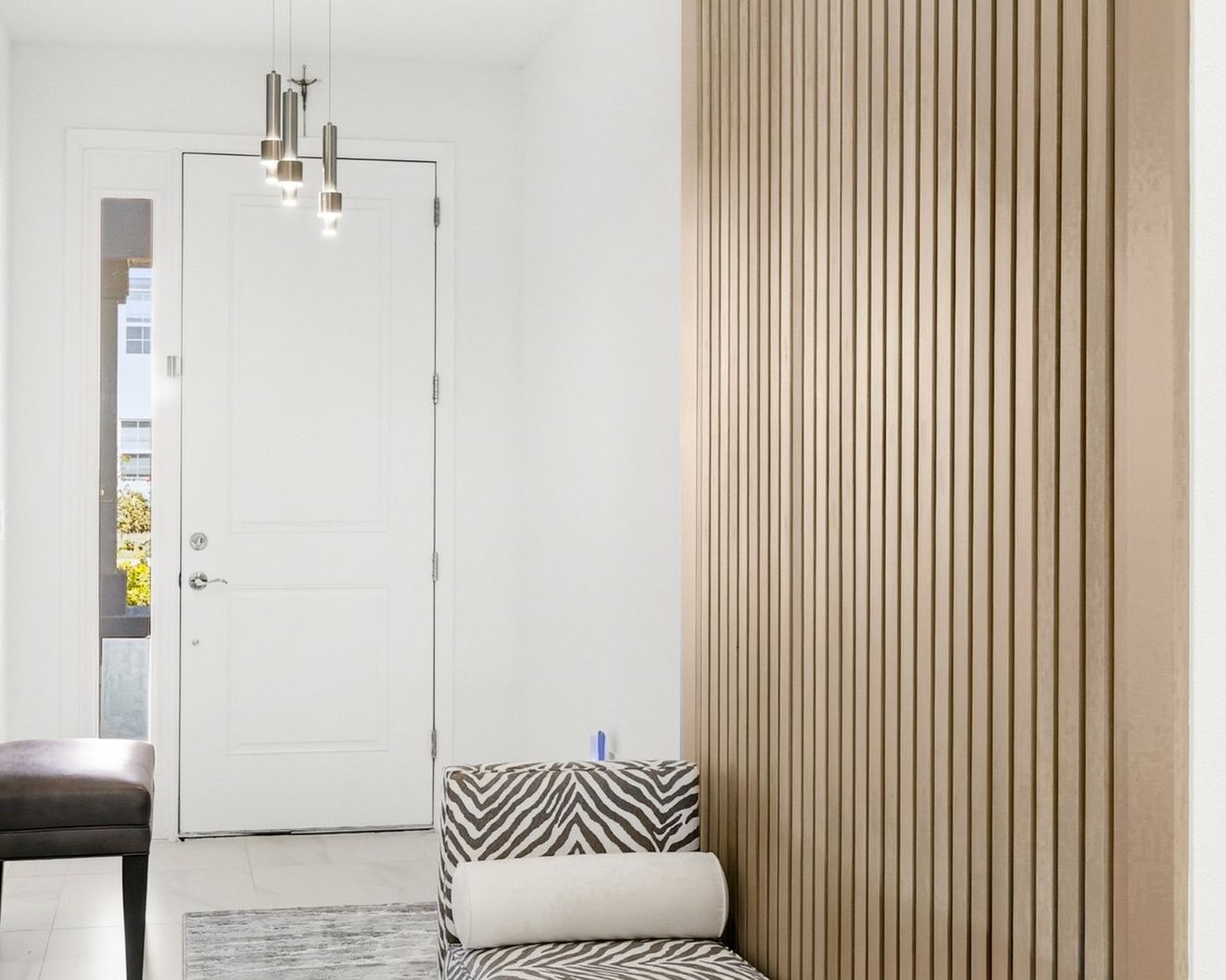 Hallway with a natural wood vertical slat wall beside a bench, looking toward a white front door