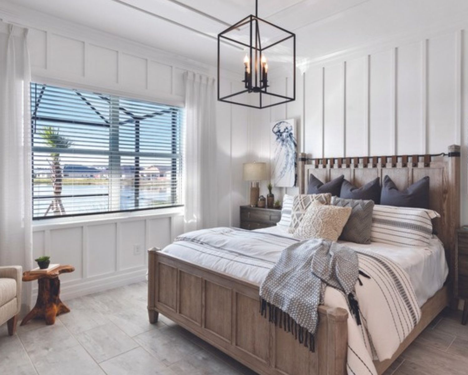 Bedroom with a white board and batten accent wall behind a wood bed, a black lantern pendant and a window to the lanai