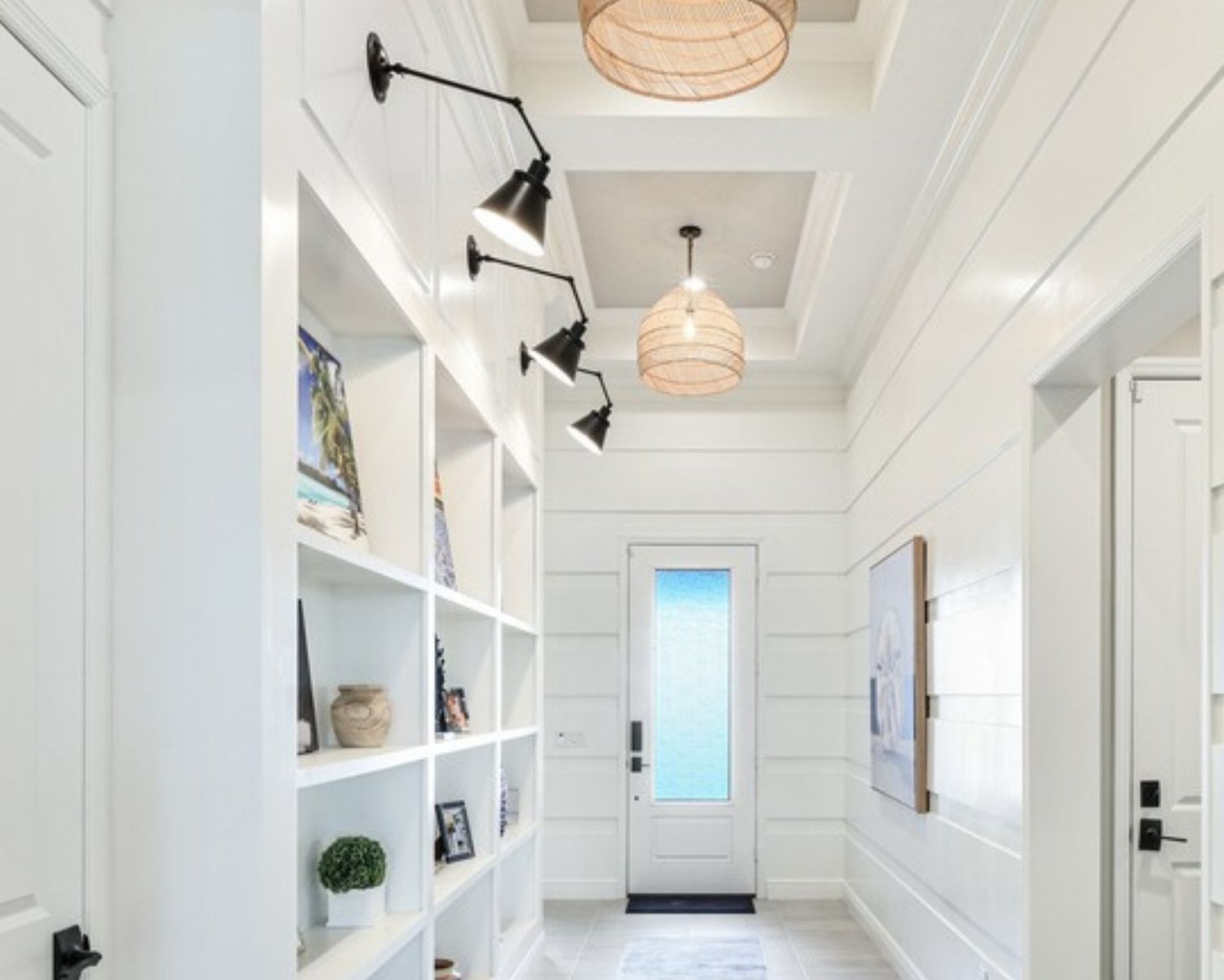 Long hallway with white horizontal plank walls, built-in shelves, black swing-arm sconces and woven pendant lights