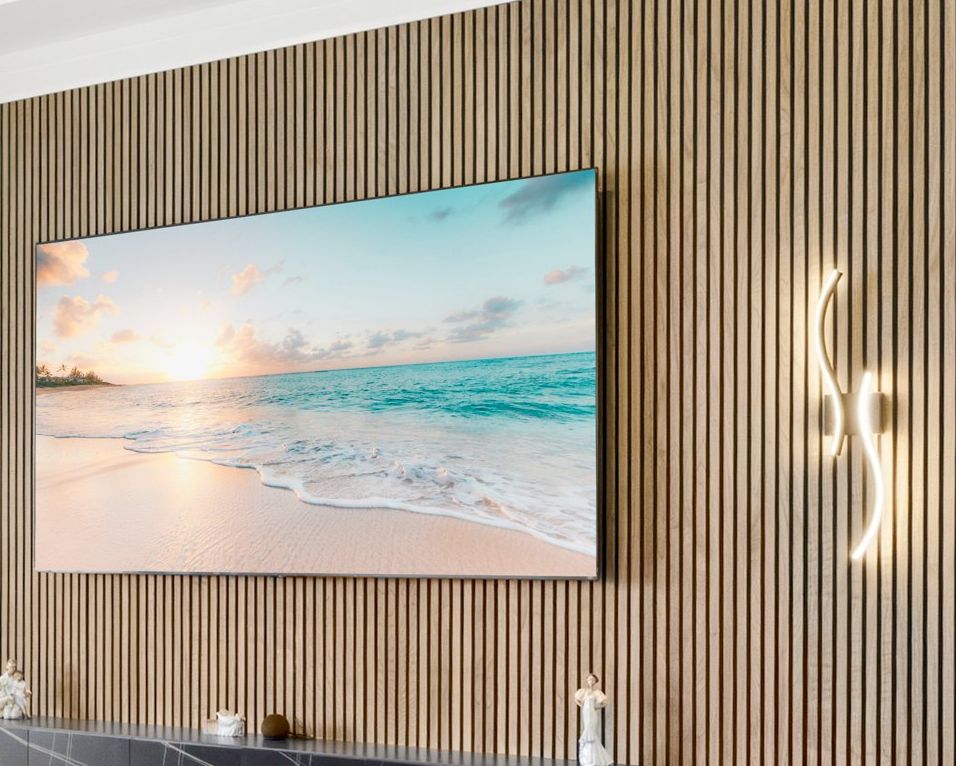 Angled close view of a natural wood slat wall with a glowing sculptural sconce beside a wall-mounted TV above a floating console